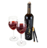 The metallic bottle pens are leaning on a bottle of wine with two glasses of wine and the pens have written on the bottle and glasses.