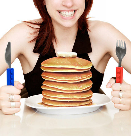 Lady eating a stack of pancakes with a red lego handle shaped fork and a blue lego handle shaped knife