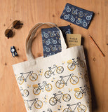 The two black bags with the bicycle designs are shown mixed with a white bag with a bicycle design lying on a wooden table.