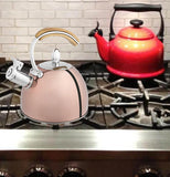 The golden tea kettle is shown sitting on a stove next to a red kettle.