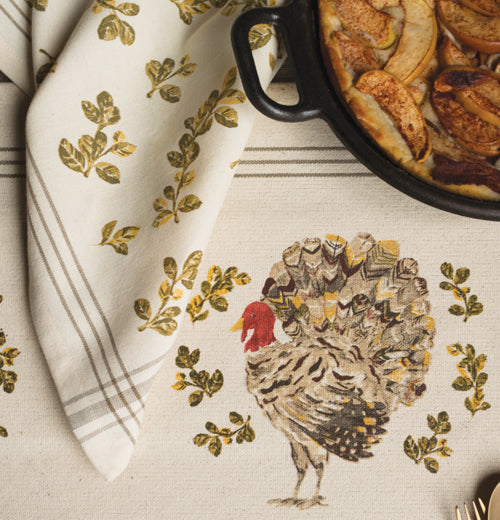 This Holiday turkey dish towel is cream colored and has a pot full of food on the dish towel.