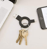 Charge and sync keychain laying on a desk between a phone and a laptop with a set of keys attached to it.