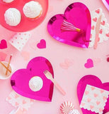 Three pink heart-shaped plates are shown with a tassel, a fork, and a white and pink napkin on them.