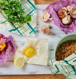 A close up of five of the food wraps on a marble cutting board with food wrapped in them like mushrooms, cilantro, lemons, and orange bell pepper