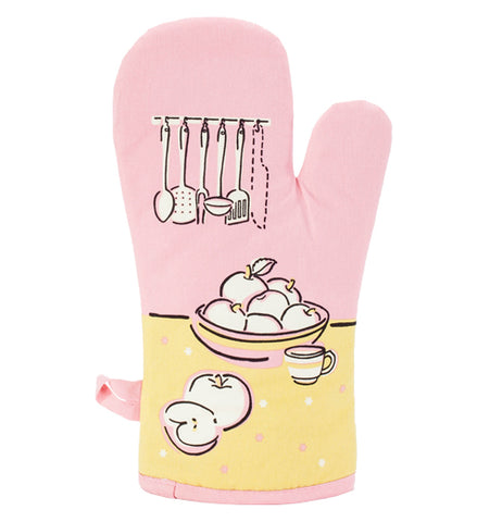 The pink oven mitt has pictures of kitchen utensils, a bunch of apples, and teacup on a yellow table.