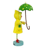 The girl figurine dressed in the yellow raincoat and holding the umbrella is shown from a side angle.