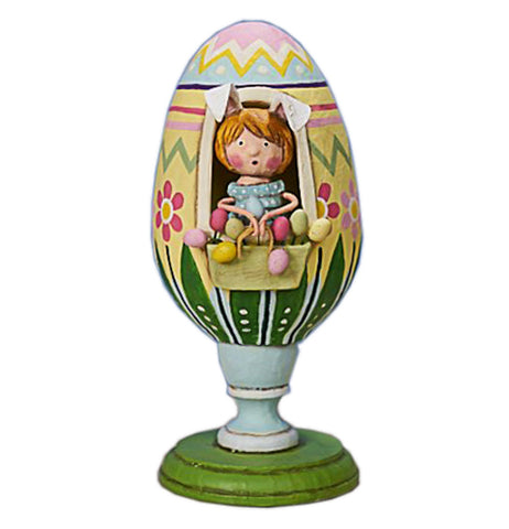 This colorful figurine has a girl in bunny ears wearing a blue dress and sitting in a large yellow, green, blue and pink Easter egg with red and pink flowers on a green pedestal.