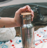 A person's hand is shown removing the lid from a steel water bottle.