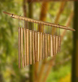 A softwood wind chime is hung by a wire frame. It has 16 chimes sorted from largest to smallest. A wooden bar helps to hang them. The background is a forest.