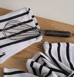 An egg beater is shown lying on top of the white towel with black stripes on a wooden table.