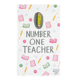 Yellow enamel pencil pin with #1 Teacher written on it.  It's attached to a post card decorated with school related pictures.
