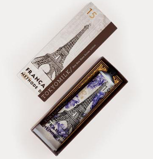 French Kiss shea butter lotion inside a tube container that contains the picture of the Eiffel Tower and purple flowers on the exterior of the tube inside of the open box which contains the picture of the Eiffel Tower and the words Tokyo Milk and " Bon Bon Shea Butter Lotion" along with the number 15