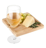 Some grapes and cheese are shown sitting on the wooden board. A wine glass is shown attached to the slot shape in the board.