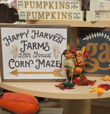 a display of a lot of box signs, on of the "Corn maze" sign with a couple "Pumpkins" sighs and a couple figurines, on of a bow in a turkey costume and the other of a girl in a native american costume, its thanksgiving themed