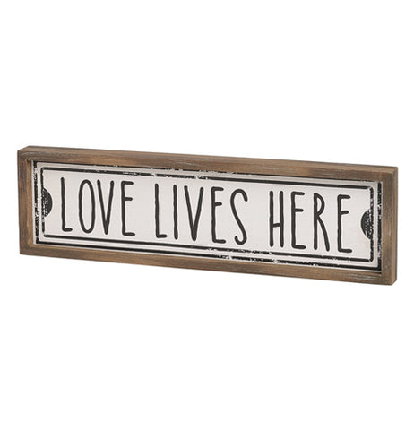 The "Lives Here" Street Sign features the message that reads, "Love Lives Here" in black over a white background surrounded by rectangular brown wooden frame. 