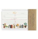 This set of white recipe cards feature a design of potted plant, books, and fruit bowls at the bottom of the paper. They are shown in their packaging with the words, "Rifle Paper Co. Recipe Cards" in black lettering.