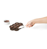 Some cookie dough is shown being spread into the cylindrical slots of the baking dish.