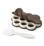 This plastic mold has 10 cylindrical shapes to put ice cream scoops in so as to make small ice cream sandwiches. It also comes with a silicone lid to provide cover when baking miniature cookies. A white plastic spatula is shown lying next to the baking dish.