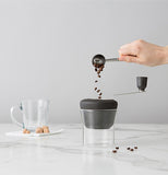 The coffee beans are shown being dumped into the open hole at the top of the grinding lid.