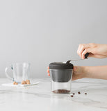 The handle is shown being turned clockwise to grind the beans down into the cup.