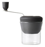 This tool has a rotating black handle and a grinding mechanism inside its black lid that fits over a big transparent glass cup.