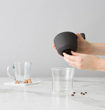 The lid is taken off the glass cup and the hole where the ground up beans come out of is visibly shown.