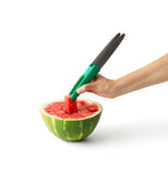 The tongs part of the slicer tool are shown picking up a cube-shaped piece of watermelon.