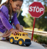 A little girl playing with a plastic school bus with a stop sign in the back ground.