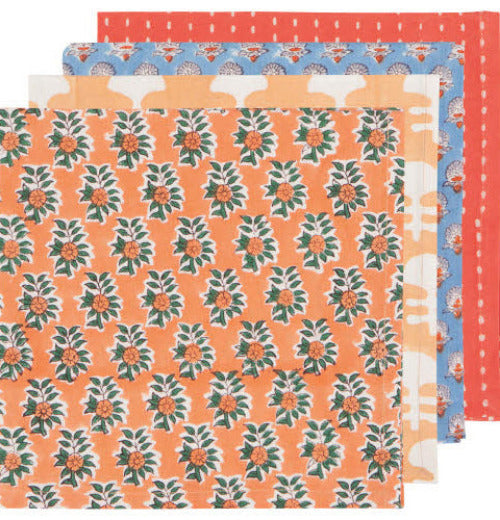 Four napkins overlapping each other in a stack. The first napkin is orange with a orange flower with green leaves. The second napkin is orange with white splotches. The third napkin is blue with white and orange flowers. The fourth napkin is red with white dots.