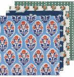 Four napkins overlapping each other in a stack. The first napkin is light blue with dark blue, orange, and white flowers. The second napkin is blue with white splotches. The third napkin is white with green and orange flowers. The fourth napkin is green with white dots.