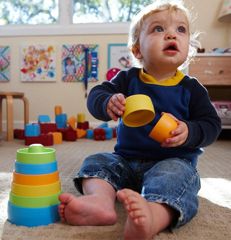 A baby is shown playing with the multi-colored stacking cups.