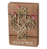 Green, pink, and white cactus string art with "Wild & Free" in white on wood over a white background.