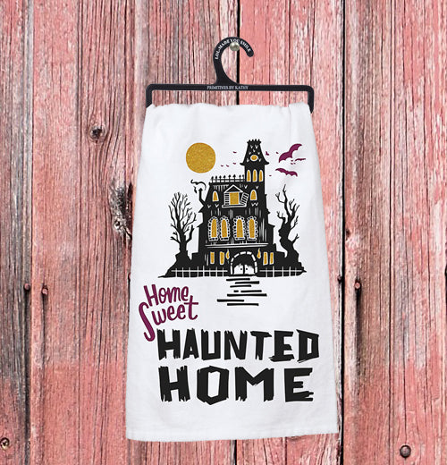 The "Home Sweet Haunted Home" dish towel hangs on a pink wooden wall. 