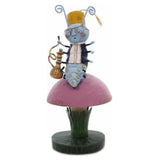 A light blue caterpillar in black coat and white shirt wearing a hat and glasses sitting on a toadstool holding a gold hookah.
