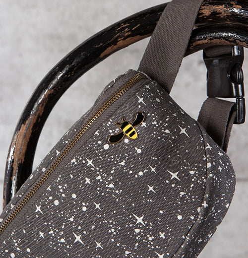 An enamel pin of a black and yellow honeybee attached to a black fanny pack with a white star design.